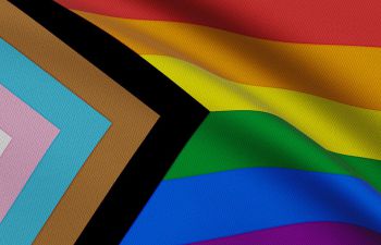 A close up of the progress pride rainbow flag which includes stripes in the trans pride colours and black and brown stripes.