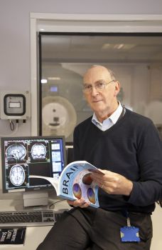 A photo of Prof Nigel Leigh from BSMS sat in front of a scanner holding a book