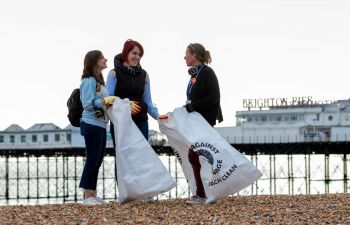 Two students taking part in a beach clean with Kelly Coate, PVC for Education and Students. They are holding white bags with the Surfers Against Sewage Logo.