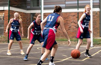 women basketball players in red and blue kits playing on a basketball court