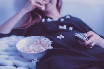 Woman eating popcorn smiling with popcorn and TV remote in foreground