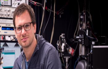 Professor Tom Baden looking directly at the camera, with machines behind him