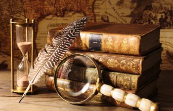 image of medievel looking books, a feather and magnifying glass