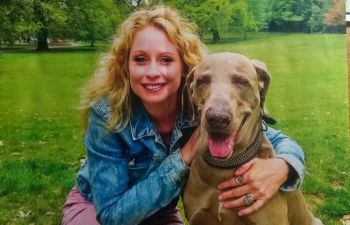 A smiling Rebecca kneels on grass with her right arm around a seated weimaraner on the cover of the latest edition of the journal 'Professional Social Work'