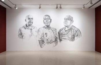 3 large black and white portraits sketched onto a white wall. A black woman centre, 2 black men each side.  Her face is conveying a mix of strength and vulnerability, intricate charcoal strokes create a compelling and emotive portrayal of the subject.