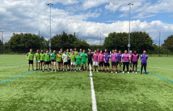 staff and students football teams on the football pitch before the match having a group photo taken