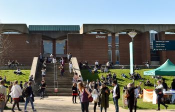 Groups of students walking around library square and chatting, with stalls in the background