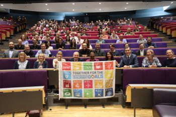 Business School staff seated in a lecture theatre hold the United Nations Sustainable Development Goals flag