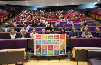 Business School staff seated in a lecture theatre hold the United Nations Sustainable Development Goals flag