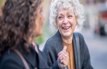 An image of an older woman and a younger woman sitting together, chatting. Both are smiling.