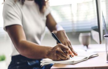 An image of a woman writing in a notebook with a pen.