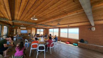 Young people, parents, teachers and menstrual health experts are pictured in a wooden cabin sitting at tables and discussing in workshop groups.