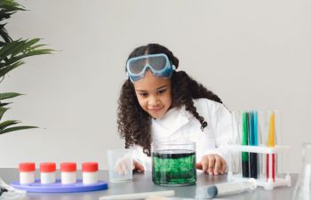 A black girl in a lab coat is playing with food colouring in test tubes