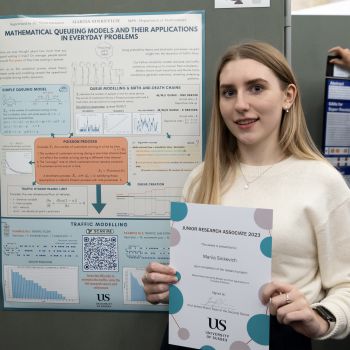 Young lady holding a certificate in front of a large poster in an exhibition hall