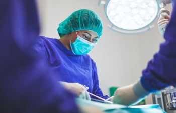 A woman in blue scrubs operating in a surgical theatre