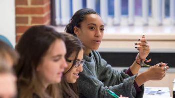 Female student in focus, hands gesturing, in a classroom with other students