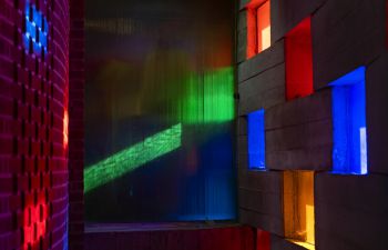 Sunlight shining through multi-coloured glass windows onto a brick wall.