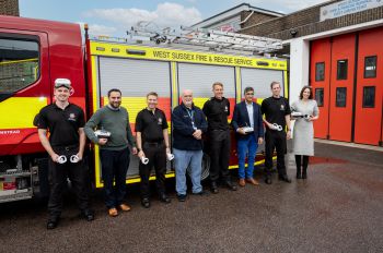 A group of people stood in front of a fire engine in a line, some wearing VR headsets