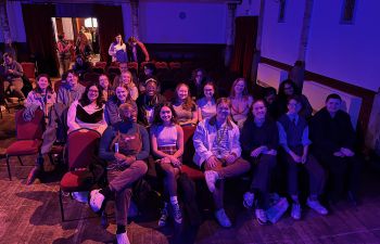 A group of about 20 students sitting in the Stanley Arts theatre, smiling at the camera.