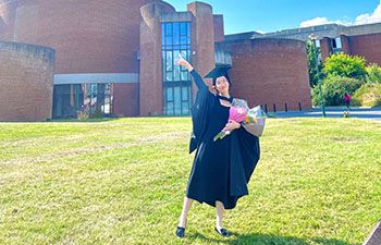 Manni Li celebrating her degree result outside the ACCA building, holiding her hand in the air and holding a bunch of flowers on a sunny day
