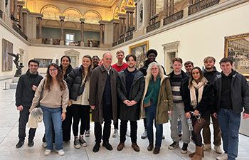 Students and staff with alumnus Paul Wright (centre) visiting the Magritte Museum standing inside the museum in the gallery