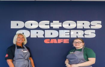 two baristas standing in front of cafe sign