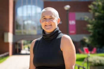 Kate O'Riordan stands smiling in front of Falmer House on a sunny day.