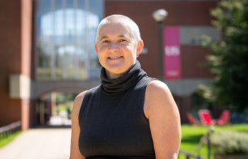 Kate O'Riordan stands smiling in front of Falmer House on a sunny day.