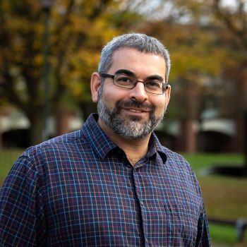 Robin Banerjee smiles in focus, in front of a blurred campus background