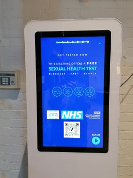 A vending machine mounted to a wall with a blue touch screen