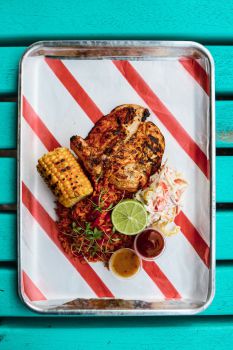 peri peri chicken, spicy rice, coleslaw, corn on the cob, spicy sauces on a metal tray with striped paper