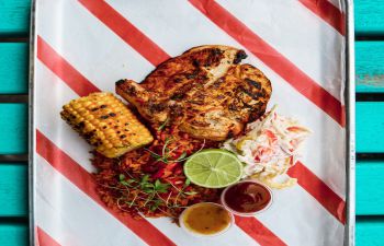 peri peri chicken, spicy rice, coleslaw, corn on the cob, spicy sauces on a metal tray with striped paper