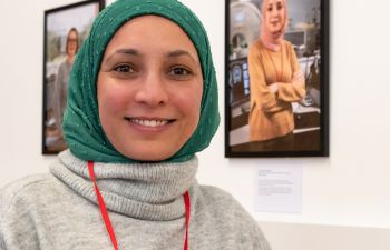 A Sussex colleague wearing a green headscarf in front of her picture which is part of the exhibition at the Library