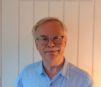 Dr Andrew Morgan wearing glasses and a blue shirt and smiling at the camera