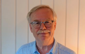 Dr Andrew Morgan wearing glasses and a blue shirt and smiling at the camera