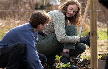 Two young females smile at each other while kneeling down to plant