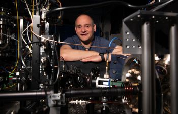 Professor Winfried Hensinger crossing his arms behind a prototype of a quantum computer in the quantum technologies lab at the University of Sussex