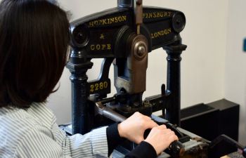 A woman uses a vintage printing press.
