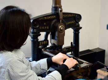 Photo of a person with black hair using an old printing press.