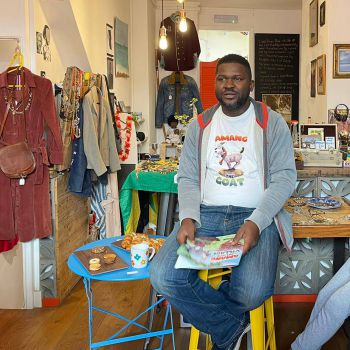 Photo of Namse Udosen, a Black masc person seated in a shop.