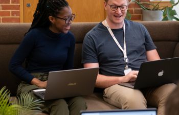 Two students smiling and using their laptops