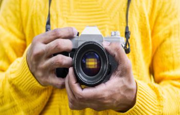 A person wearing a yellow jumper holding a camera