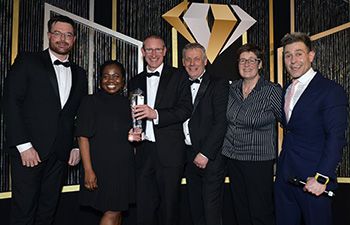 l-r Alex Maltsev and Jemima Aryee presenting the award to Chess Dynamics, with comedian Simon Brodkin.