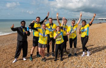 Team Sussex at the Brighton Marathon standing on Brighton beach wearing yellow Sussex t-shirts