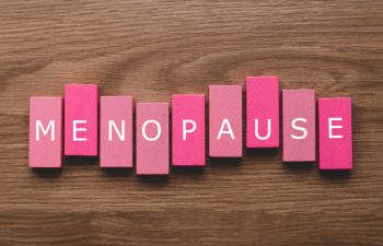 letters spelling menopause on pink background