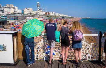 Four students stood in a line looking at a view of Brighton beach in the sunshine.