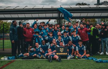 The Sussex men's football team celebrating their win with a varsity winners banner