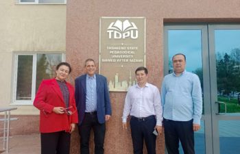 Four people stand in front of a building with a plaque showing that it is the Tashkent State Pedagogical University. Marcelo stand second in from the left.