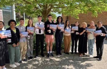 A group stands in the sun outside Essex House holding certificates