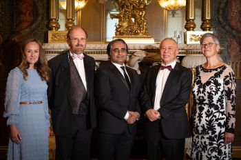 Group of people in front of an ornate fireplace, wearing evening wear and smiling towards the camera